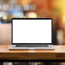 Laptop blank screen on wooden table in coffee shop morning sunshine background